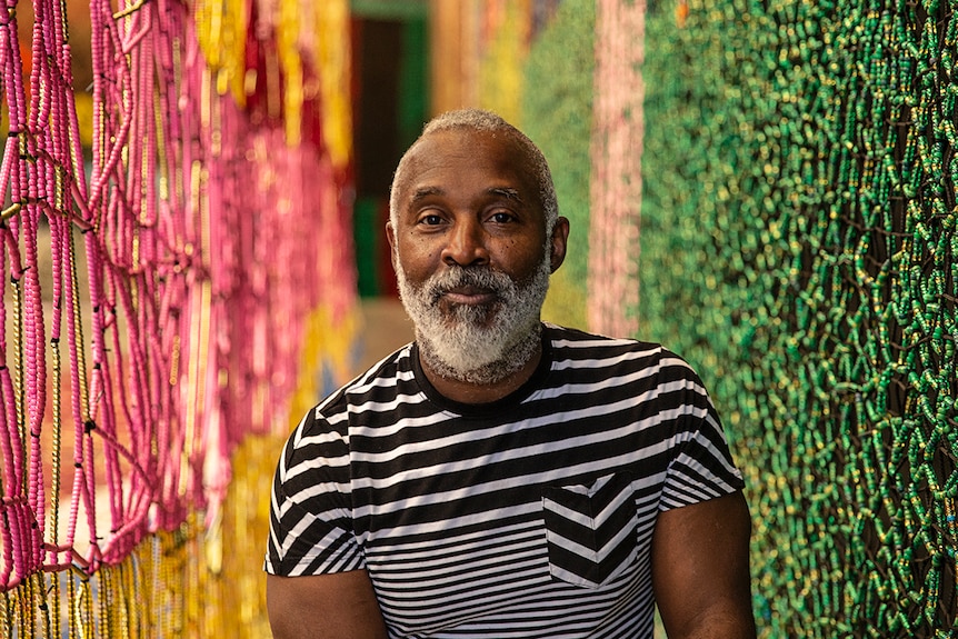 Colour photo of artist Nick Cave in front of artwork Beaded Cliff Wall.