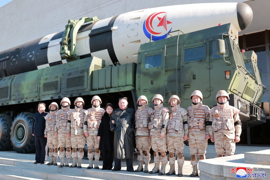 Kim Jung Un and his daughter standing between ten soldiers in front of a missile