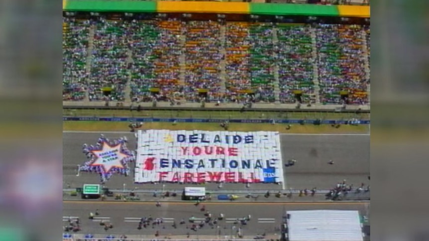 Archival vision of a race track with an enormous banner in front of the grandstand saying 'Adelaide You're Sensational Farewell'