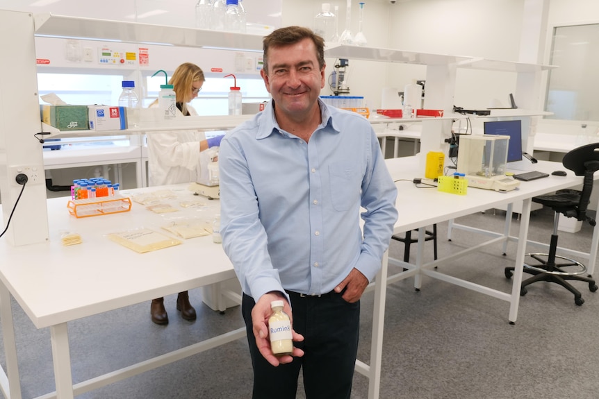 A man holds a bottle of product in front of him in a laboratory.