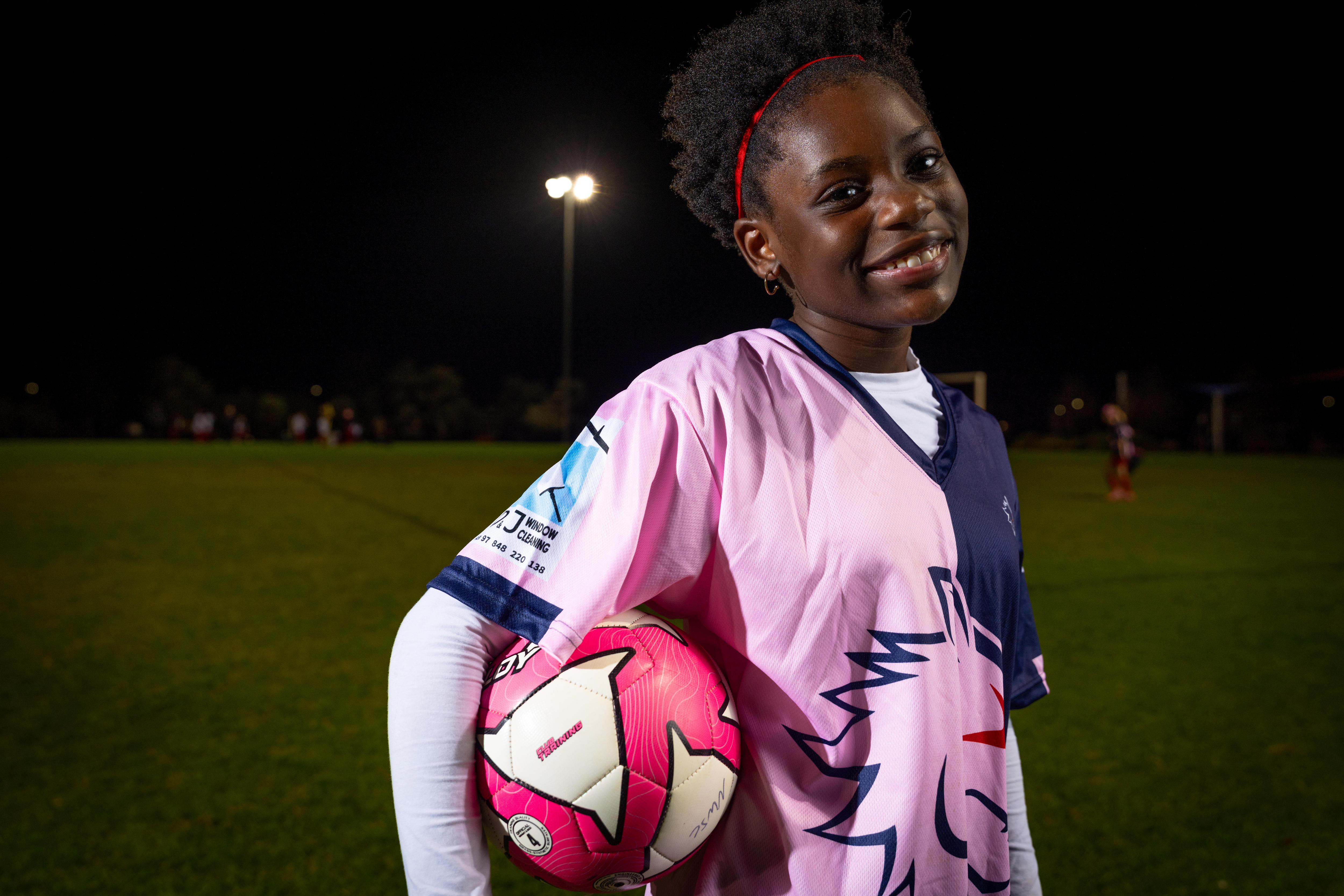 A girl holds a soccer ball to her hip while smiling.