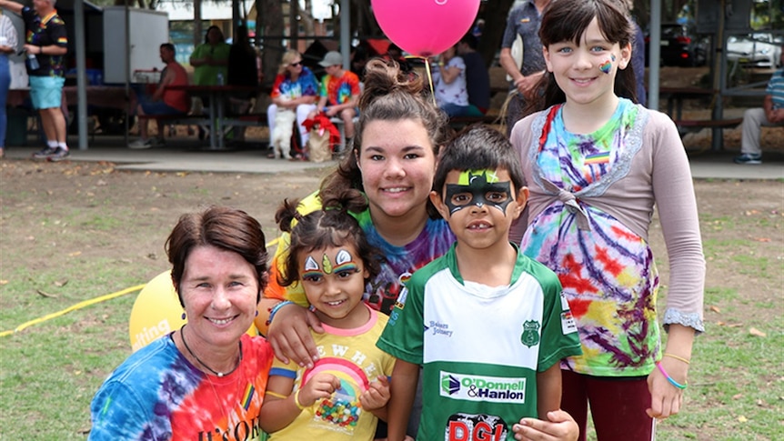 A smiling woman wearing a rainbow tie-dye top with young children in rainbow clothing