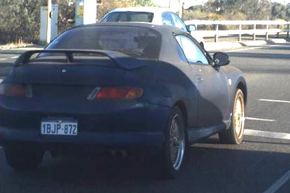 A photo of a blue Mitsubishi Coupe driving on the road, taken from behind the vehicle.