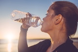 Woman drinking from water bottle against sunset