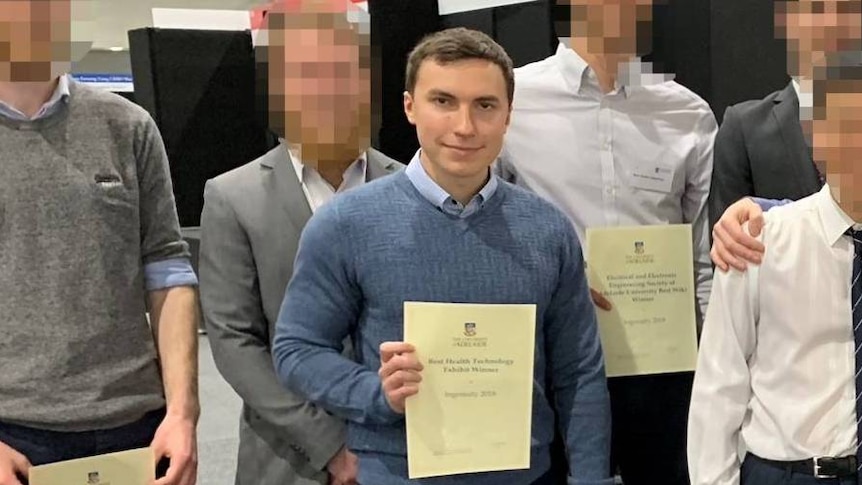 A group of people hold up university certificates. All faces are blurred except the man in the middle.