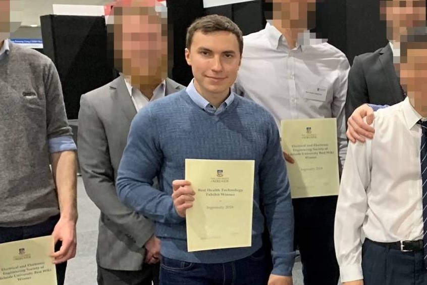 A group of people hold up university certificates. All faces are blurred except the man in the middle.