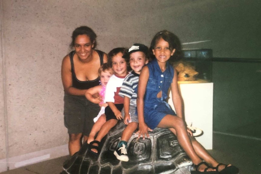 A mother and four children smile for the camera, while sitting on a model of a giant tortoise