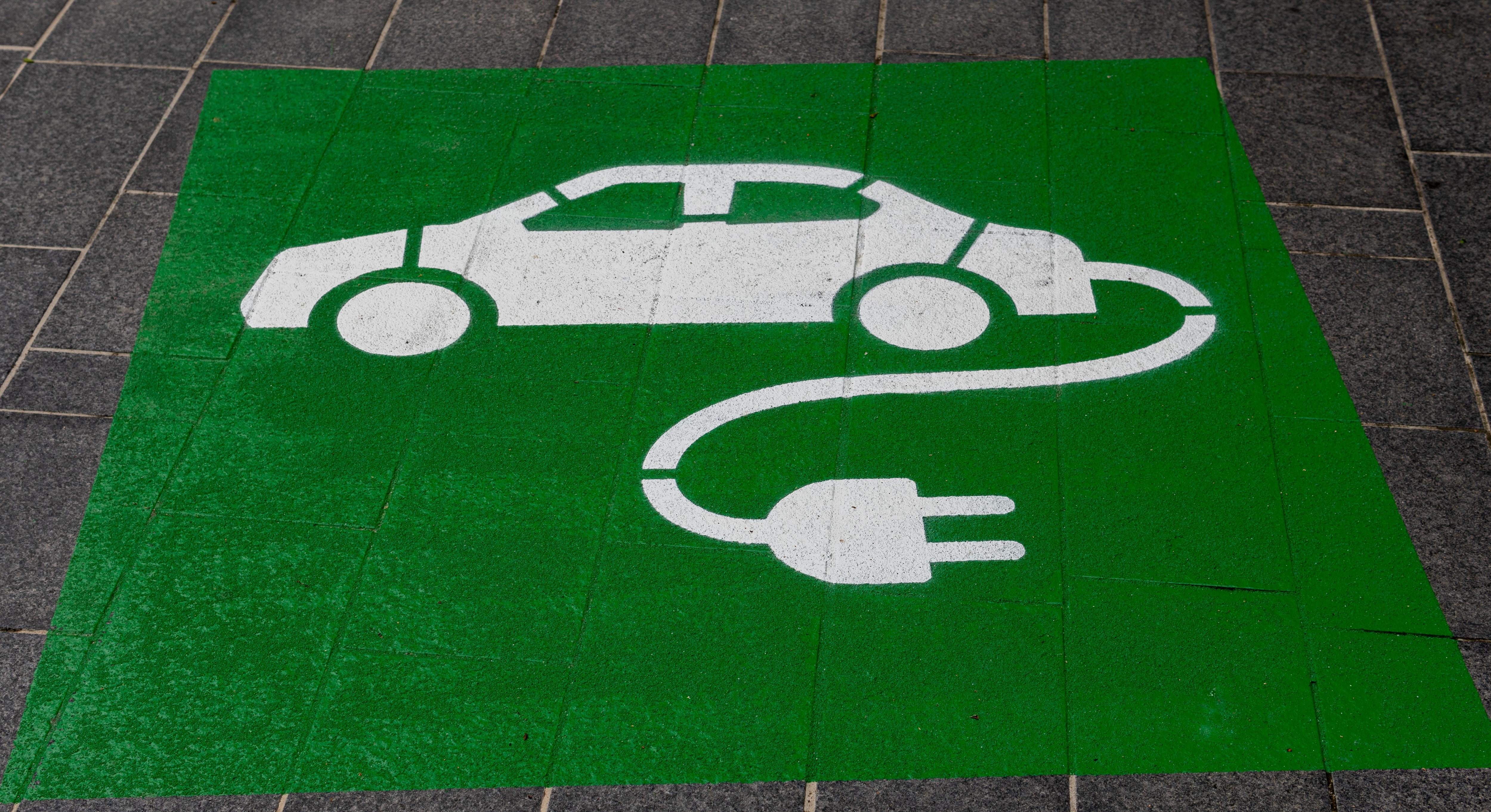 A painted image of a white car, with an electrical cord attached, on a green background. 