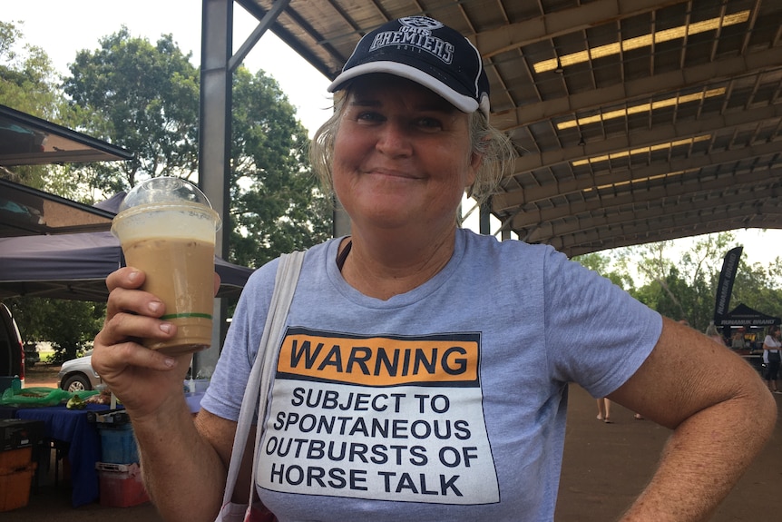 a woman wearing a cap and a shirt holding an iced coffee