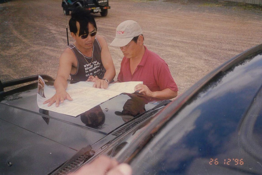 Archival image of two men looking at maps on the bonnet of a car.