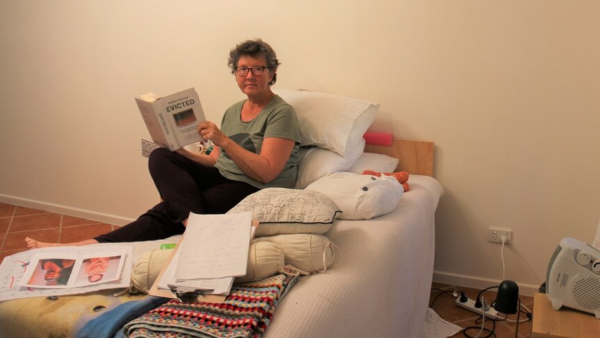62-year-old Anne Margaret O'Connor sits on bed reading book 'Evicted'