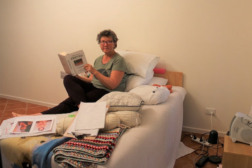 62-year-old Anne Margaret O'Connor sits on bed reading book 'Evicted'