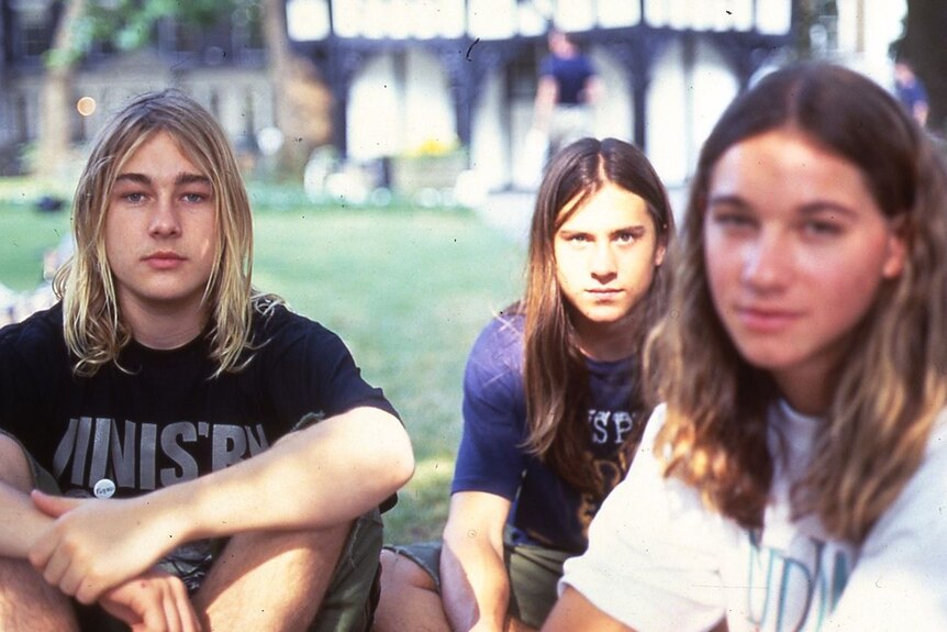Three teenagers with long hair sit in a park