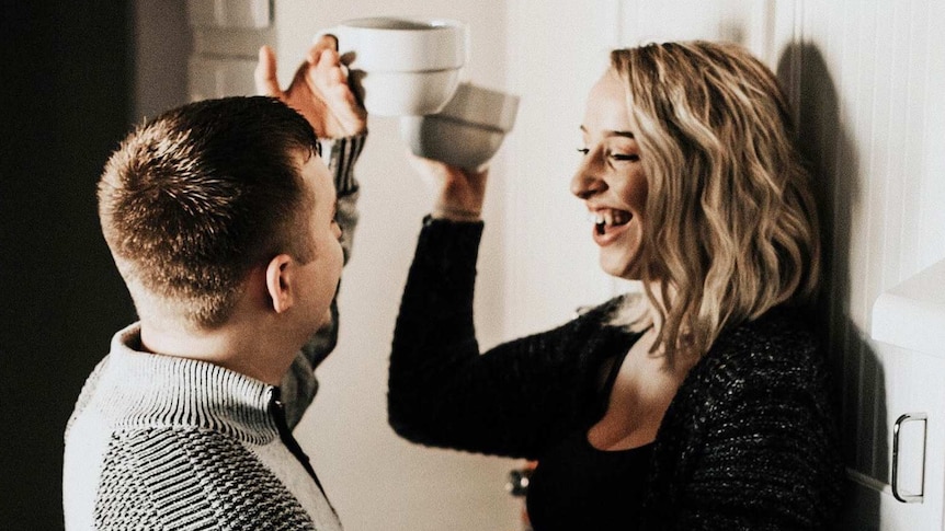 Man and woman in the kitchen laughing together for a story about evening up the household chores at home for better equality.