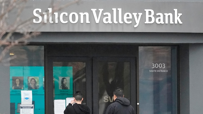 People stand outside the doors of a grey building which says Silicon Valley Bank.