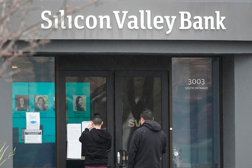 People stand outside the doors of a grey building which says Silicon Valley Bank.