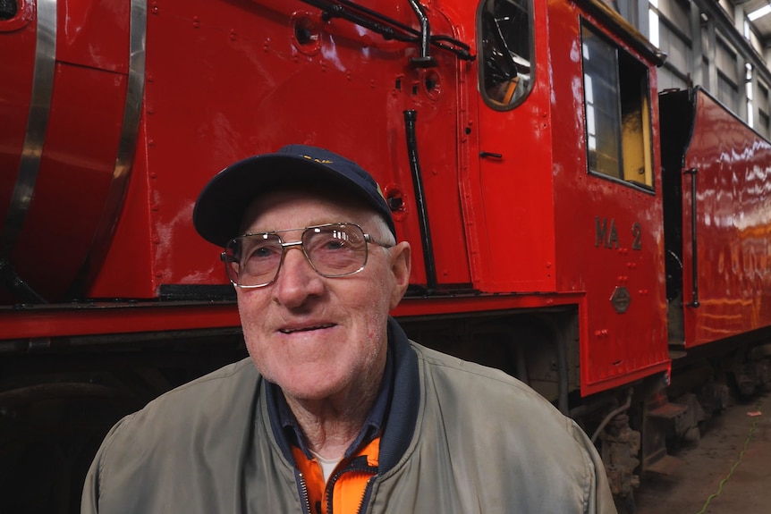 Elderly man smiling in front of huge red steam train.