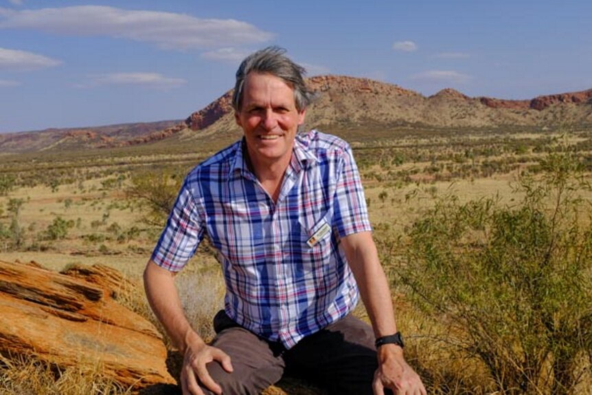 A man crouches with the Australian desert in the background.