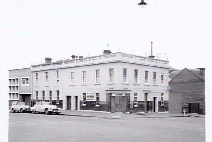 A large white hotel on a street corner, with old cars parked out front.