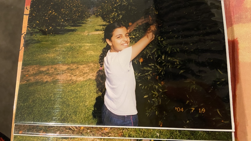 girl smiling at the camera while she picks oranges from a tree