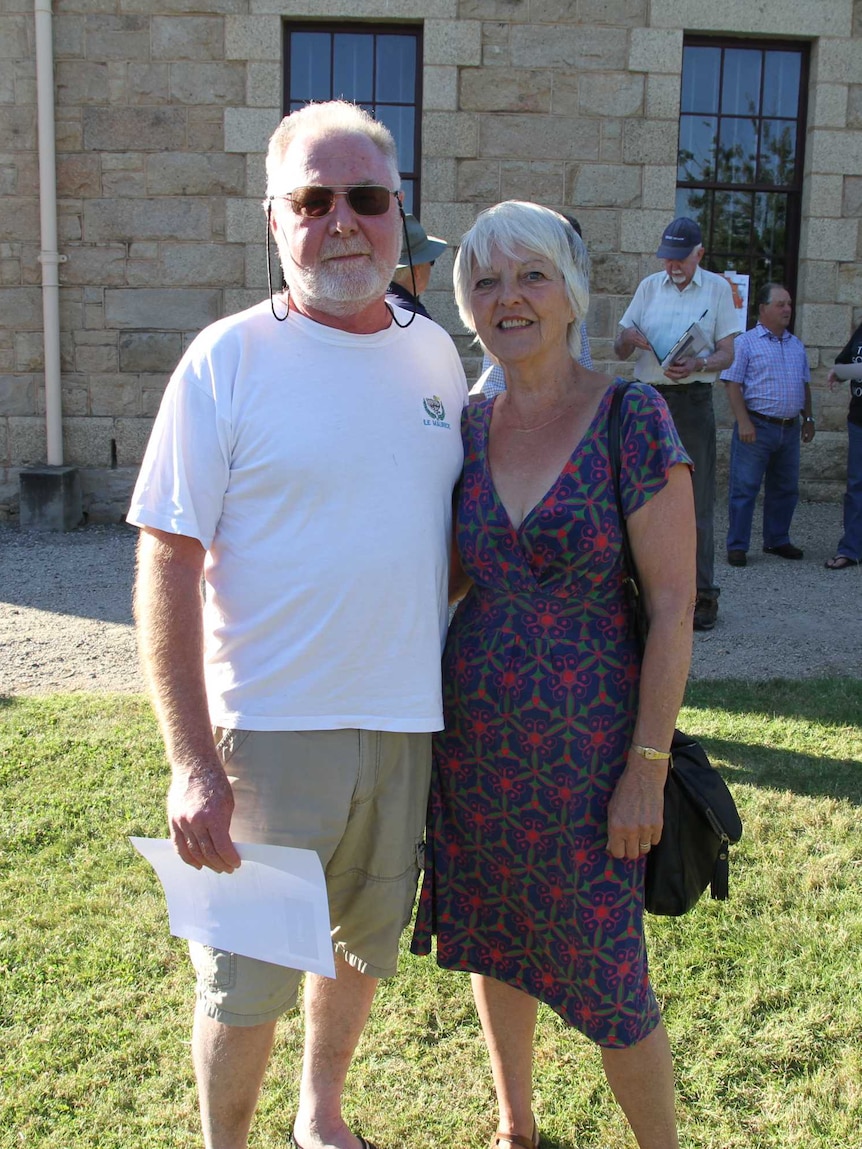 man with white beard in shorts and t-shirt next to woman in purple dress