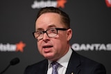 A close up of Alan Joyce pictured in front of a Qantas backdrop