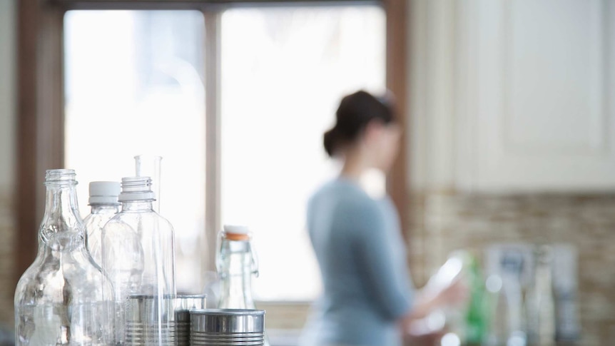 Bottles and cans on a kitchen bench, with a woman in the background