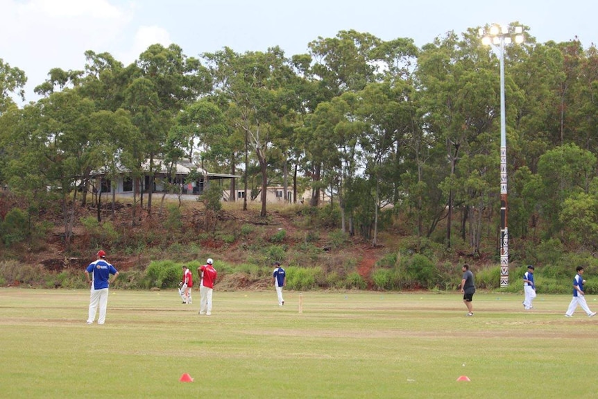 Some cricketers standing around a makeshift cricket pitch, beneath oval tower lights, in Yirrkala.