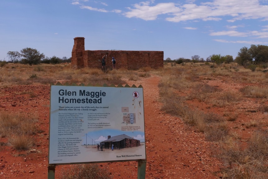 A sign for the Glen Maggie Homestead, with the ruins of the homestead itself in the background.