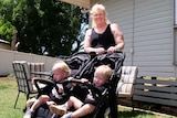 woman in black shirt pushes blonde toddlers in pram
