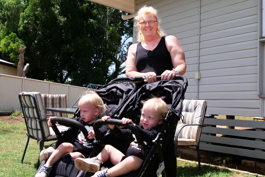 woman in black shirt pushes blonde toddlers in pram
