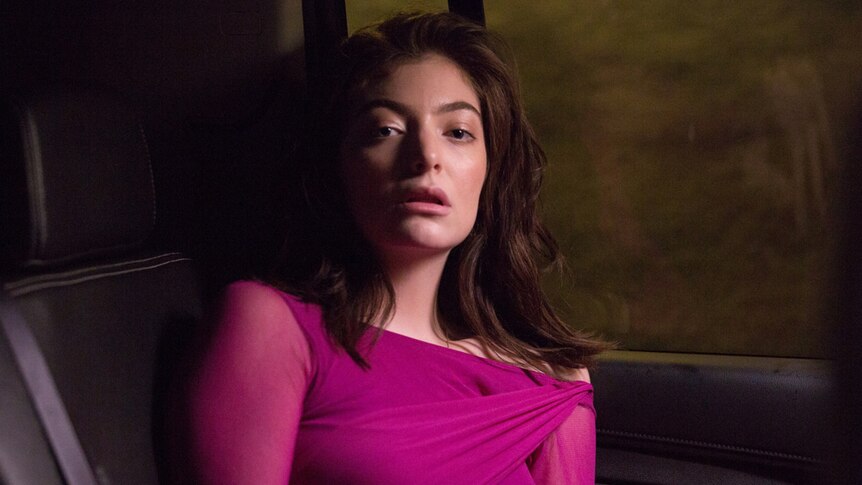 Lorde wearing a pink dress and sitting in the back seat of a car