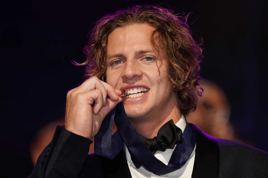 A smiling Nat Fyfe bites then Brownlow Medal as it hangs around his neck.