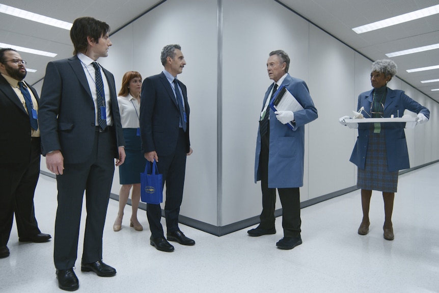 Office workers stand in the hallway with white walls. 