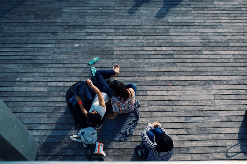Three university students sit on decking on campus.