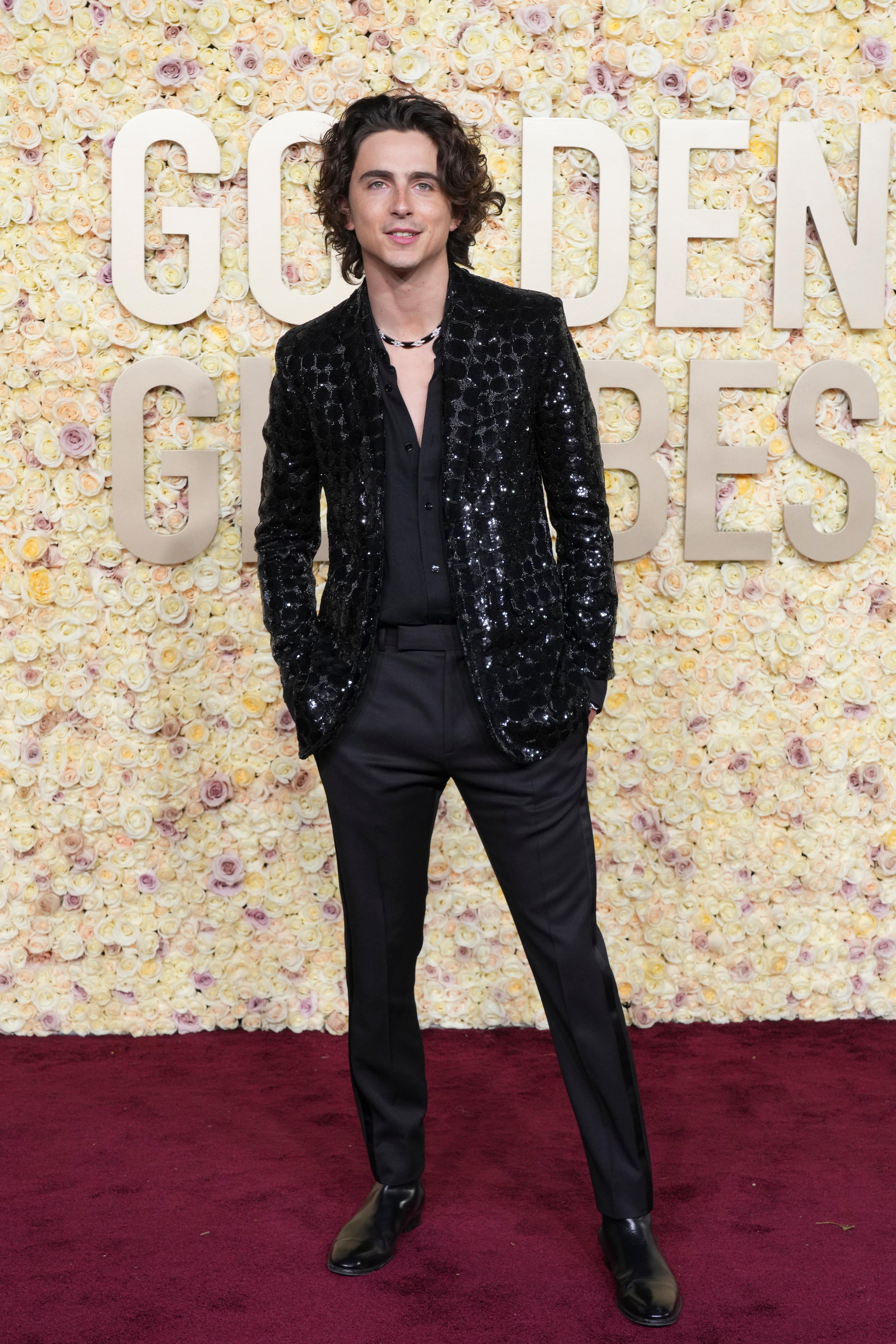 Actor Timothee Chalamet wearing a black suit with a shiny jacket