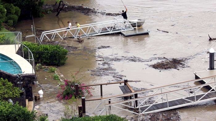 Debris in the Brisbane River flows around pontoons of residences in St Lucia