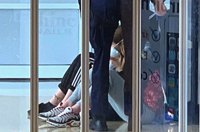 A police officer visible through clear panels in a security gate, the officer bending over two young people sitting down