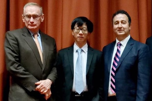 Three men standing in suits in front of orange curtain