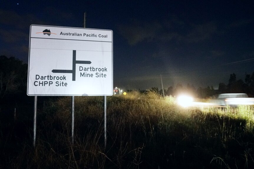 A road sign showing where the Dartbrook mine site is at night with cars going past blurred.