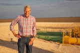 Man stands on drought-stricken property, with barren land in the background.