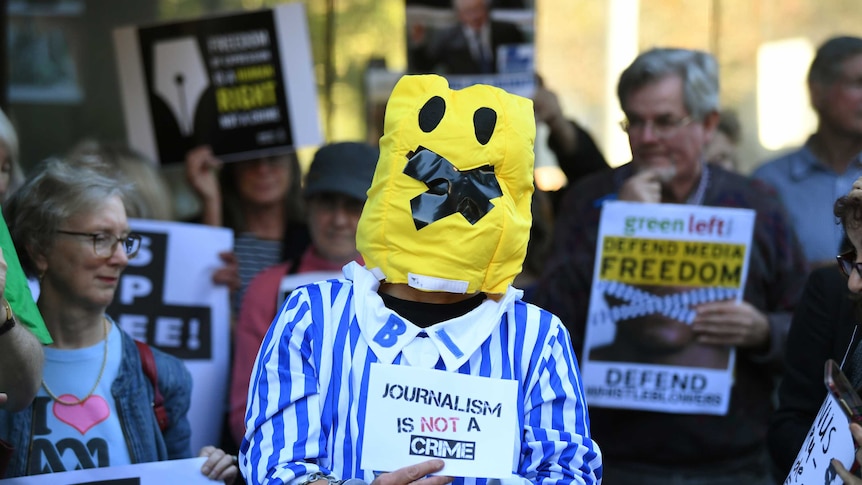 A person dressed as a banana with tape over its mouth holds a sign.