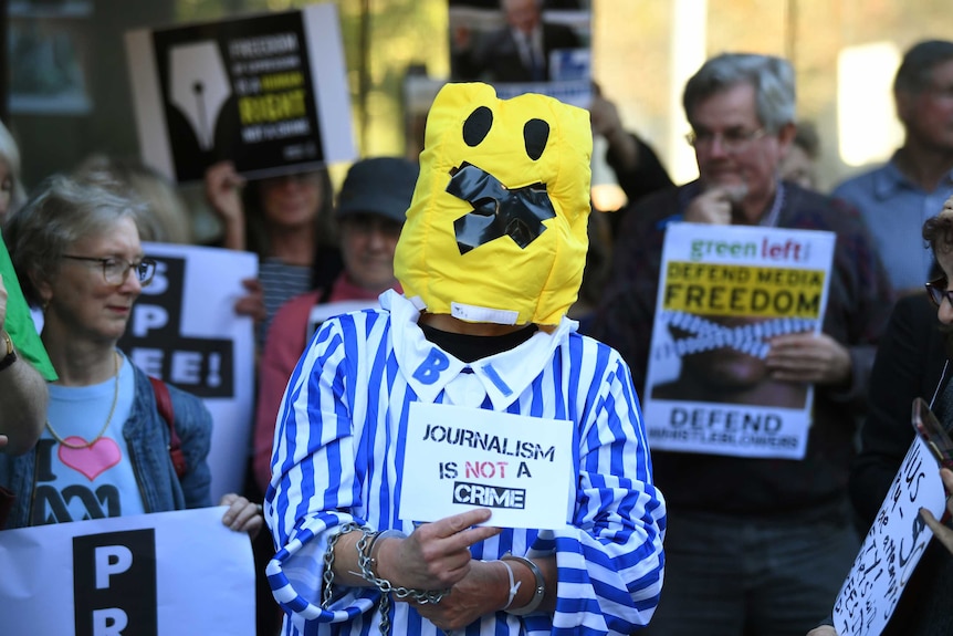 A person dressed as a banana with tape over its mouth holds a sign.