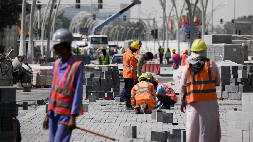 Several construction workers wearing hi-vis vests and helmets work on a paved street