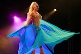 a drag queen singing on stage is a large flowing dress with lights behind her