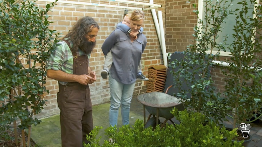 Man and woman with child on her back, looking at plants in a garden