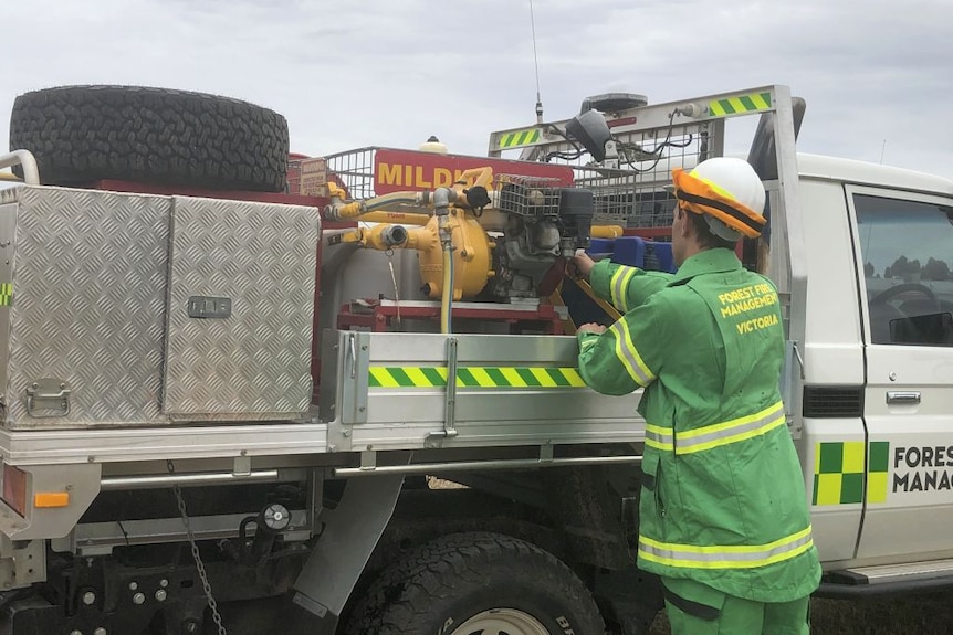 A firefighter recruit adjust a pump on the back of a ute.