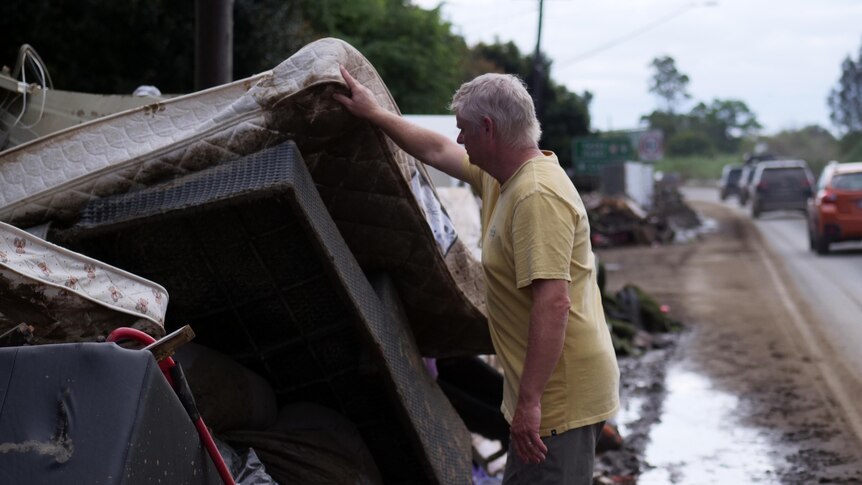 A man inspects a flood damaged mattress on the side of a road