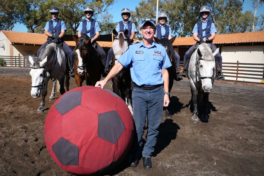 Police on horseback pose in a stables with a giant soccer ball toy