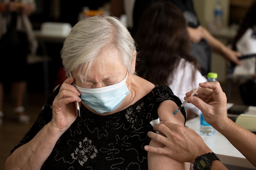 An Israeli woman talks on her phone as she receives a third coronavirus vaccine injection